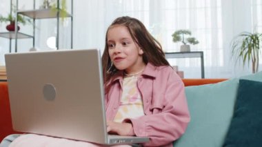 Dizüstü bilgisayar kullanan mutlu kız çocuğu, iyi haber mesajı alıyor, ani zaferle şoke oluyor piyango galibiyetini evde online alışveriş yaparak kutluyor. Yaşam tarzı teknolojileri.