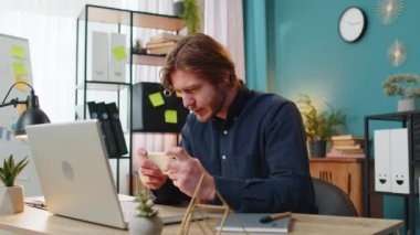 Genç serbest çalışan teneffüste dinleniyor ve iş günü akıllı telefondan online video oyunları oynuyor. Adam hevesle oyun oynuyor ya da akıllı telefondan video oyunu oynuyor masada oturuyor..