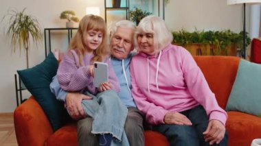 Beyaz tatlı bir kız oturma odasındaki kanepede akıllı telefon kullanarak dedeme ve büyükanneme ders veriyor. Büyükannem ve büyükbabam, torunumun cep telefonuyla oyun oynamasını izliyorlar. Hafta sonu evde mutlu bir aile.