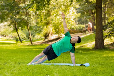 Mutlu Asyalı Japon adam parkta egzersiz yapıyor, yoga yapıyor, spor antrenmanlarını minder üzerinde yapıyor. Aktif Çinli sporcu güneşli yaz gününde sağlıklı yaşam tarzının tadını çıkarıyor. Genç adam egzersiz yapıyor..