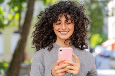 Kafkas 'lı genç bir kadının sosyal medya uygulamasında akıllı telefon kullanarak kısa mesajlar yazarken, internette sörf yaparken, dinlenirken, dışarıda mola verirken. Şehir sokağındaki kadın. Güneşli park