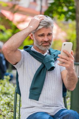 Akıllı telefon daktilosu kullanan sakallı, olgun bir adam, beklenmedik piyango sonuçlarını kaybeder, kötü haber, servet kaybı, başarısızlık. Şehir caddesinde duran bir turist. Kasaba yaşam tarzları.