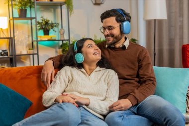 Evdeki kanepede dans eden kablosuz kulaklıklı neşeli, genç çift en sevilen disko rock n roll müziğini dinliyor. Gülümseyen rahat aile hafta sonunun tadını çıkarıyor..