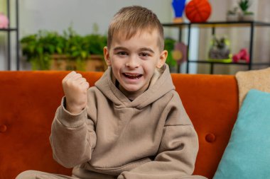 Mutlu çocuk bağırıyor, başarıyı kutluyor, kazanıyor, gol başarısı, iyi haber, piyango şansı, zafer, modern ev dairesinde televizyon şampiyonluğu seyrediyor. Oyun odasında kanepede oturan genç bir çocuk.