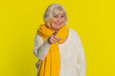 Seni seçiyorum. Kıdemli gülümseyen kadın kamerayı işaret ediyor ve neşeli bir ifadeyle bakıyor, kazanan seçimi yapıyor, yön gösteriyor. Yaşlı büyükanne sarı arka planda izole edilmiş.