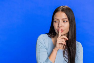 Sessiz olun lütfen. Genç bir kadın işaret parmağını dudaklarına bastırıyor sessizlik işareti yapıyor. Gizli saklı konuşmayın, dedikoduyu kesin. Çekici kız mavi stüdyo arka planında tek başına. Metin için kopyalama alanı