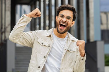 Mutlu heyecanlı Hintli girişimci bağırıyor, başarıyı kutluyor, kazanıyor, gol başarısı, iyi haber, piyango talihi, açık havada zafer. Şehirdeki Arap Hindu adam. İş adamları