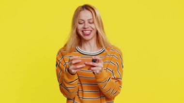 Mutlu, heyecanlı, sarışın, yarış pilotu simülatörü oyunu oynayan sarışın kadın akıllı telefonda video oyunu oynuyor. Kız oyuncu sarı arka planda büyük ikramiyeyi kazandı.