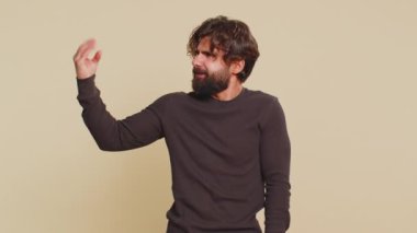 Hintli genç adam, elleri, yuvarlanan gözleri, dedikoduları, boş vaatleri vs vs saçma sapan jestler yapıyor. Yalancılar! Lübnanlı Hintli adam bej renkli stüdyo arka planında tek başına..