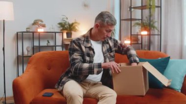 Mutsuz genç beyaz adam kutuları açıyor, kablosuz kulaklık siparişinden memnun değil, mobil uygulamalara olumsuz geri bildirim yazıyor, internet alışverişi kavramı.