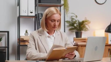 Kafkasyalı yetişkin iş kadını ilginç kitaplar okuyor, sayfaları çeviriyor, edebiyattan zevk alıyor, işten sonra dinleniyor. Laptop bilgisayarı olan ve ofis masasında dinlenen mutlu serbest çalışan kadın..