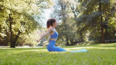 Spor giysili beyaz bir kadın parkta yoga minderiyle egzersiz yapıyor. Yetişkin bir sporcu kızın öne eğilmesi sağlıklı yaşam tarzını temsil eder. Atletik kadın çimlerin üzerinde diz çöküyor..