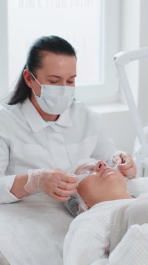 Güzellik uzmanı kadın yüzünden nemlendirici nano maske çıkarıyor. Gözlerin etrafındaki narin cildin gençleşmesi. Yaşlanma önleyici maske tedavisi kırışıklıkları, siyah daireleri, tansiyon eksikliğini, kuruluğu ortadan kaldırıyor.