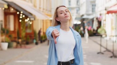 Hoşlanmamak. Kafkasyalı kadının işaret dilini göstermesi hoşnutsuzluğunu belirterek tatminsiz kötü iş hatasını dile getiriyor. Şehrin güneşli caddesinde duran hoşnutsuz kadın.