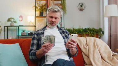 Başarılı, mutlu, son sınıf öğrencisi akıllı telefon tutuyor ve evdeki kanepede oturan banknotları sayıyor. Kafkas sakallı mutlu yaşlı adam çevrimiçi piyango oyunu kazanıyor. Bütçe kavramı hesaplanıyor.