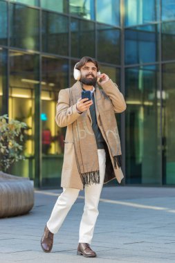 Mutlu Arap işadamı kablosuz kulaklık takıyor, açık havada akıllı telefondan en sevilen enerjik müziği dinliyor. Gülümseyen adam şehir sokağının yanından geçiyor. Yaşam Tarzları.