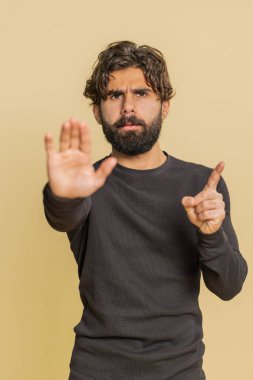 Indian man says No hold palm in stop gesture, warning of finish, prohibited access, declining communication, body language, danger. Young Hispanic Hindu guy on beige background. People lifestyles. clipart