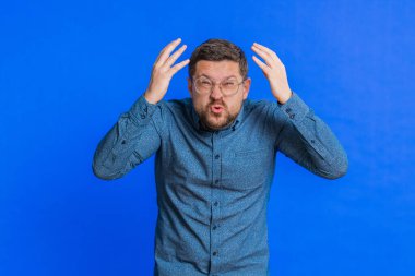 Kafkasyalı üzgün yetişkin bir adam umutsuzluk, yalnızlık, sinir krizi, piyango sonuçlarına şaşırma, kötü şans kaybı kötü haber. Çekici genç adam mavi arka planda izole edilmiş.