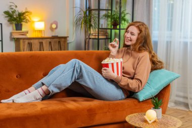 Rahatlamış kızıl saçlı genç bir kadın patlamış mısır yiyor ve evdeki oturma odasında kanepede oturup film seyrediyor. Mutlu kızıl elbiseli kız hafta sonu boyunca dairede film izlemekten zevk alıyor..