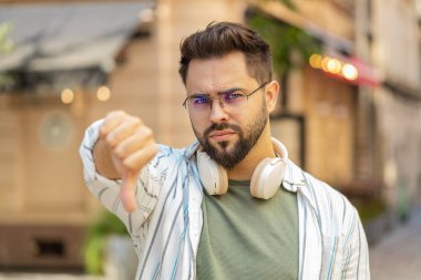 Hoşlanmamak. Kafkasyalı genç adam işaret dilini gösteriyor, hoşnutsuzluğunu dile getiriyor, tatminsiz kötü işler yapıyor, açık havada hata yapıyor. Şehir caddesinde duran hoşnutsuz turist..