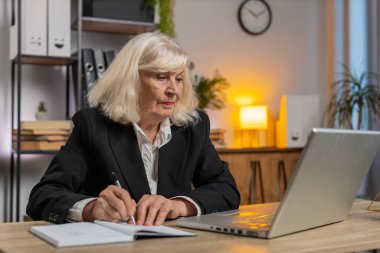 Üst düzey iş kadını, internet video dersine ya da ofis masasındaki bilgisayar toplantısına katılırken not alıyor ya da not alıyor. Kız bağımsız büyükanne destek hizmetleri webcam 'e bakıyor.