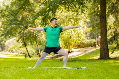 Genç sporcu şehir parkında jimnastik yapıyor. Sportif Japon erkek dışarıda yoga yapıyor. Formda sporcu, ormanda kas germe egzersizleri yapıyor..