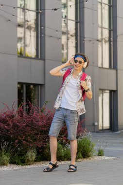 Kablosuz kulaklıklı, dans eden, açık havada en sevilen enerjik disko müziğini dinleyen mutlu, rahat, beyaz bir adam. Kıvırcık saçlı ve sırt çantalı neşeli turist şehirde yürüyor..