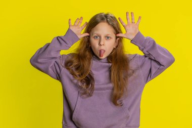 Komik, genç, kızıl liseli bir kızın portresi kameraya surat yapıyor, şakalaşıyor, aptal suratıyla şakalaşıyor, alay ediyor, taciz ediyor. Sarı arka planda reşit olmayan çocuk.