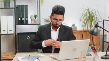 Stresli Hintli işadamı, modern ofis çalışma masasında çalışırken göğsünde kalp krizi geçirme riski bulunan gerilimden muzdarip. Resmi takım elbiseli erkek Hindu.