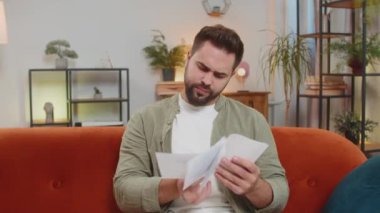 Stresli esmer adam oturma odasında ödenmemiş banka borçlarına bakıyor evrak işleri, planlama bütçesi ipotek ödemelerini hesaplıyor, son teslim tarihini hesaplıyor. Erkek adam eve kağıt para atıyor..