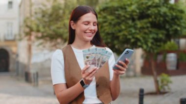 UAH Ukrayna Hryvnias paralarını hesaplayan mutlu bir kadın planlanmış tatil hediyeleri için gerekli gelire sahip akıllı telefon hesap makinesi uygulamasını kullanıyor. Şehir caddesinde duran güzel kız. Dışarıdaki yaşam tarzları