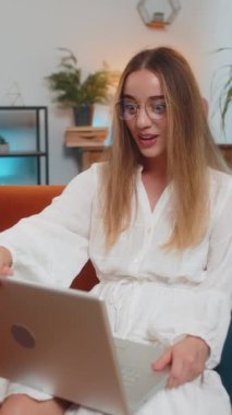 Laptop kullanan, gülümseyen, iyi haber mesajı alan, piyango ikramiyesinin beklenmedik zaferini kutlayan, rüzgar gibi saçları olan beyaz bir kadın. Dikey.