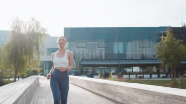 Yorgun atletik koşucu kadın akıllı saat düzeneği bileziğine bakar kalp atışlarını, nabzını, koşudan sonra SPO2 'yi kontrol eder. Güneşli şehir parkında kardiyo çalışmaktan yorgun düşmüş genç bir kadın.