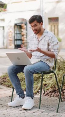 Hintli adam sandalyede oturuyor, laptop kamerasına bakıyor, arkadaşlarıyla, ailesiyle ya da müşterisiyle görüntülü bir konferans görüşmesi yapıyor, uzak sohbetin tadını çıkarıyor. İspanyol adam netbook kullanıyor. Dikey