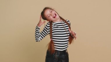 Neşeli, komik, genç, sevimli kız kameraya surat asıyor, şakalaşıyor, aptal suratıyla maymun taklidi yapıyor, alay ediyor. Bej arka planda 10 yaşında küçük bir çocuk. Küçük çocuklar