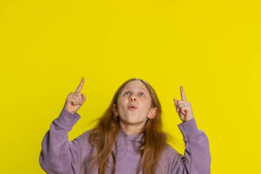 Mutlu şirin kız boş yeri işaret ediyor ticari metin için reklam alanı, ürün tanıtım afişi için fotokopi alanı. Küçük çocuk sarı arka planda kapalı alanda izole edilmiş.