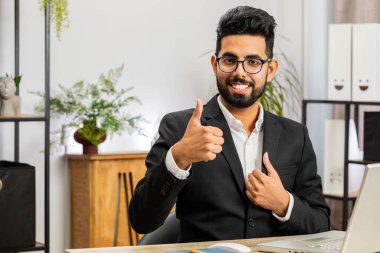 Gibi. Bilgisayarda çalışan mutlu Hintli işadamı kameraya olumlu bakıyor, olumlu bir işaret veriyor, iyi bir şey, ofis işyerindeki olumlu geri bildirim gibi. Serbest Çalışan Arap Adam