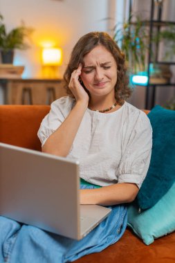 Dizüstü bilgisayar kullanan yorgun genç bir kadın, baş ağrısı, tansiyon ve migren sorunu, evde stres. Kız netbook 'ta çalışıyor, mesajlar gönderiyor, online alışverişler yapıyor, film izliyor. Dikey.