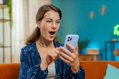 Aman Tanrım, vay canına. Heyecanlı, mutlu ve şaşırmış genç bir kadın akıllı telefon daktilo kullanarak harika bir galibiyet elde etti. Zaferi kutlamak için sınıf dairesinde kutlama yapıyorlar. Koltukta cep telefonu olan kız.