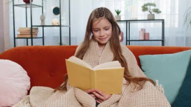 Genç beyaz çocuk battaniyeye sarılıp rahatlıyor ilginç kitaplar okuyor sayfalarca gülümsüyor edebiyat eğitiminin tadını çıkarıyor, kanepede dinleniyor. Evdeki oturma odasındaki kanepede oturan mutlu kız..