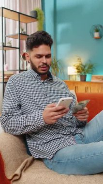 Planlama bütçesi. Zengin, mutlu Hintli bir adam akıllı telefon hesap makinesi kullanıyor. Para sayıyor, ev faturalarını hesaplıyor. Kazancından memnun olan adam, planlı tatil hediyeleri için para biriktirir.