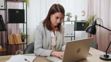 Mutlu iş kadını serbest çalışan, modern ofis çalışma masasında zafer kutlamaları yaptıktan sonra sandalyeye yaslanıyor. Resmi takım elbiseli kız evde ellerini başının arkasına koyup dinleniyor.