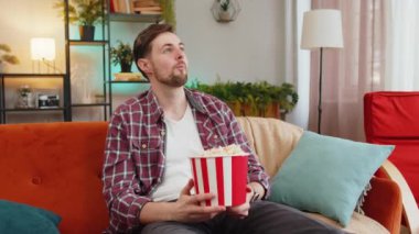 Heyecanlı bir adam patlamış mısır yiyor ve evdeki kanepede oturup ilginç TV dizileri izliyor. Ekose gömlekli mutlu beyaz adam hafta sonu boyunca film izlemekten zevk alıyor.