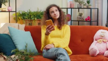 Genç kız çocuk akıllı telefon sosyal medya uygulamaları üzerinden rahatlama filmi izlerken mesajlarını paylaşıyor. Beyaz kadın, oturma odasında, koltukta otururken cep telefonu kullanıyor.