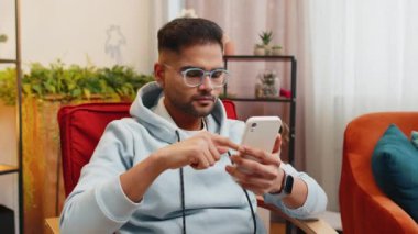 Hüzünlü Arap adam akıllı telefon daktilo kullanıyor, beklenmedik piyango sonuçlarını kaybediyor, kötü haber, servet kaybı, son teslim tarihi, virüs. Sınıftaki genç Hintli adam sandalyede.