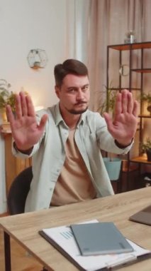 Ciddi ifadeleri olan serbest çalışan genç bir adam, iki eliyle de ofis masasında jest yapmayı kesiyor, bitiş uyarısı yapıyor, erişimi yasaklıyor, iletişimi kesiyor ve vücut dili tehlikesi var. Dikey.