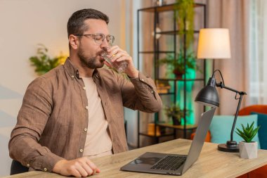 Ofis odasında dizüstü bilgisayarla çalışırken masa başında oturmuş su içen Kafkasyalı bir iş adamı. Genç erkek serbest çalışan adam bilgisayar ekranı internette geziniyor..