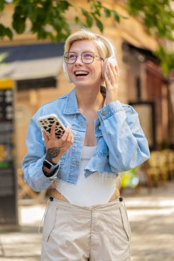 Kablosuz kulaklıklı mutlu, gevşemiş genç sarışın kız dışarıda dans eden en sevilen disko rock 'n roll müziğini dinliyor. Beyaz kadın turist şehir caddesinde yürüyor..
