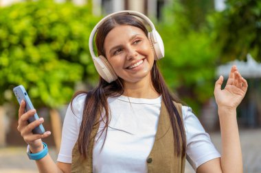Kablosuz kulaklıklar takmış, açık havada dans eden ve en sevilen disko rock 'n roll müziğini dinleyen mutlu, gevşemiş genç yetişkin kız. Şehir Güneşi Sokağı 'nda beyaz kadın..