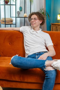 Gözlüklü yorgun genç adam rahat koltukta oturuyor, dinleniyor, gündüz uyukluyor. Kafkasyalı kaygısız beyaz adamın portresi, kıvırcık kahverengi saçlı, evinde dinlenen, kanepede dinlenen